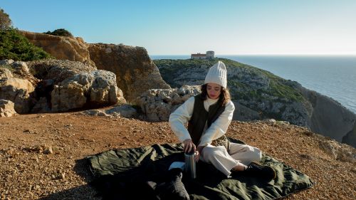 Free Woman in white beanie enjoying a cliffside picnic with ocean view, embracing nature's tranquility. Stock Photo