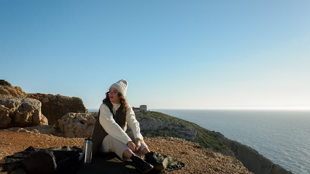A woman sits by the ocean, embracing the serene cliffside view in Lisbon, Portugal.