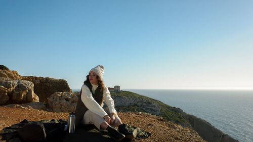 Free A woman sits by the ocean, embracing the serene cliffside view in Lisbon, Portugal. Stock Photo