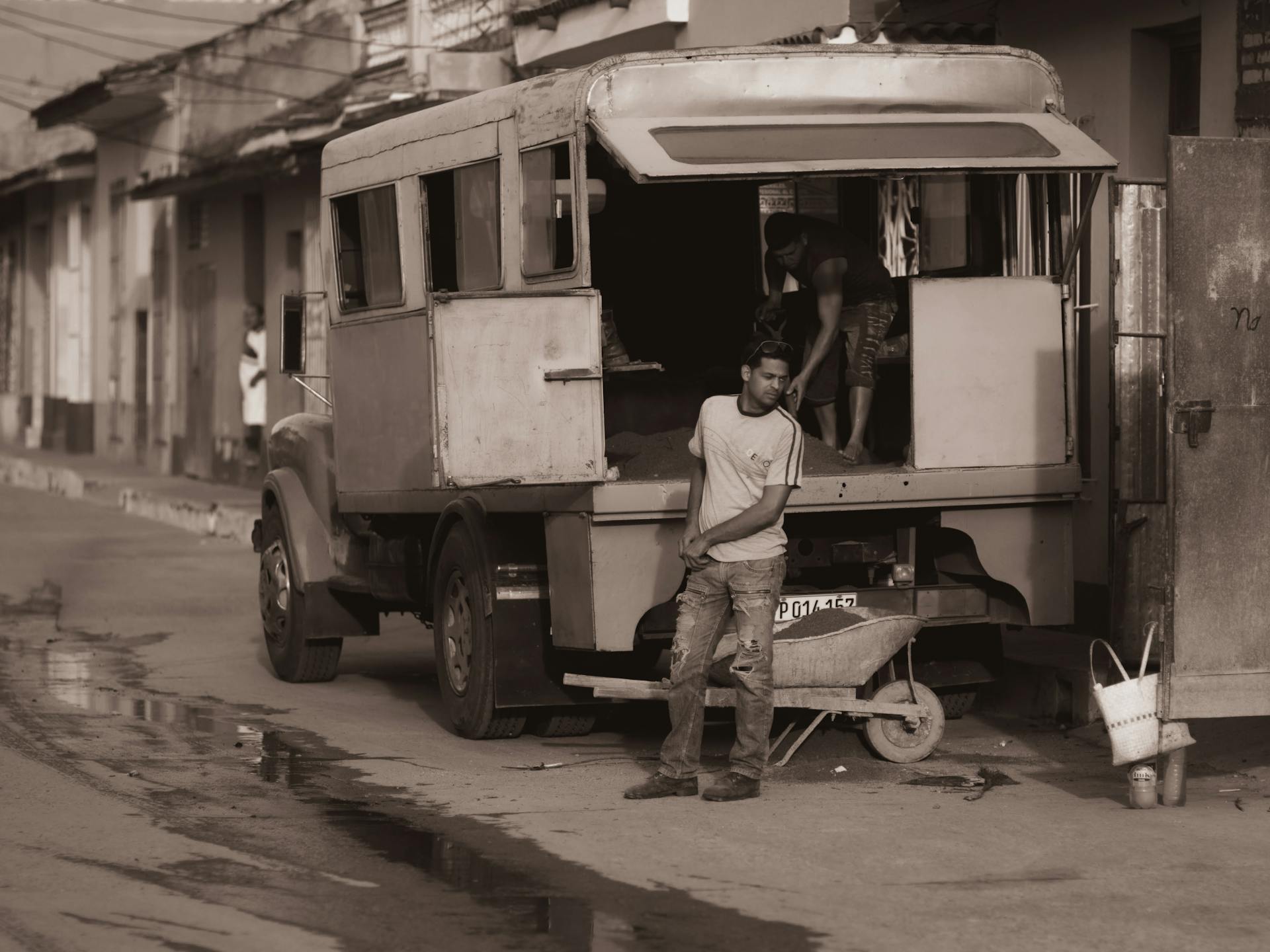 Sepia-toned image of workers by an old truck on a city street, capturing a vintage atmosphere.