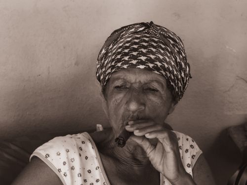 Free Portrait of an elderly woman with a headscarf smoking a cigar captured in sepia tones. Stock Photo