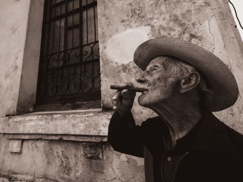 Free An elderly man with a cigar, wearing a straw hat, in a sepia-toned urban environment. Stock Photo