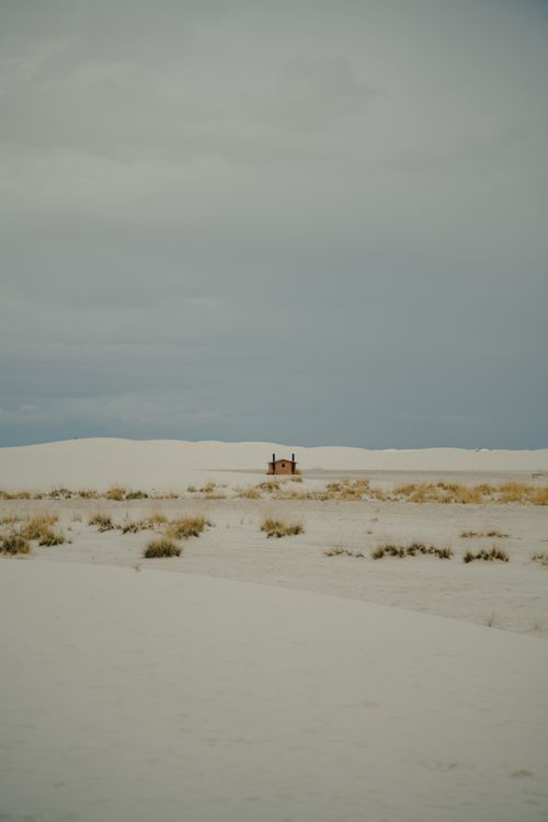 Free Lonely cabin surrounded by vast desert sands under an overcast sky, evoking solitude. Stock Photo