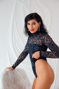 Stylish brunette posing confidently in lace bodysuit. Fashion glamour and elegance in a studio setting.