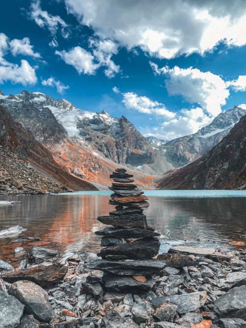 Free Balancing rock stack by a tranquil lake with mountain backdrop in Pahalgam, a serene nature escape. Stock Photo
