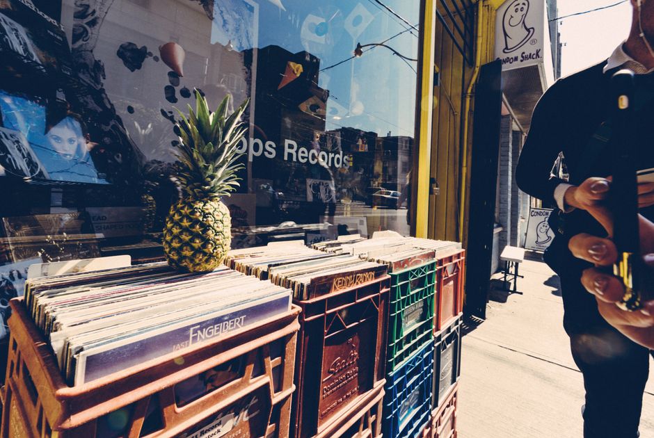Street scene with a pineapple on record crates and a person using a smartphone.