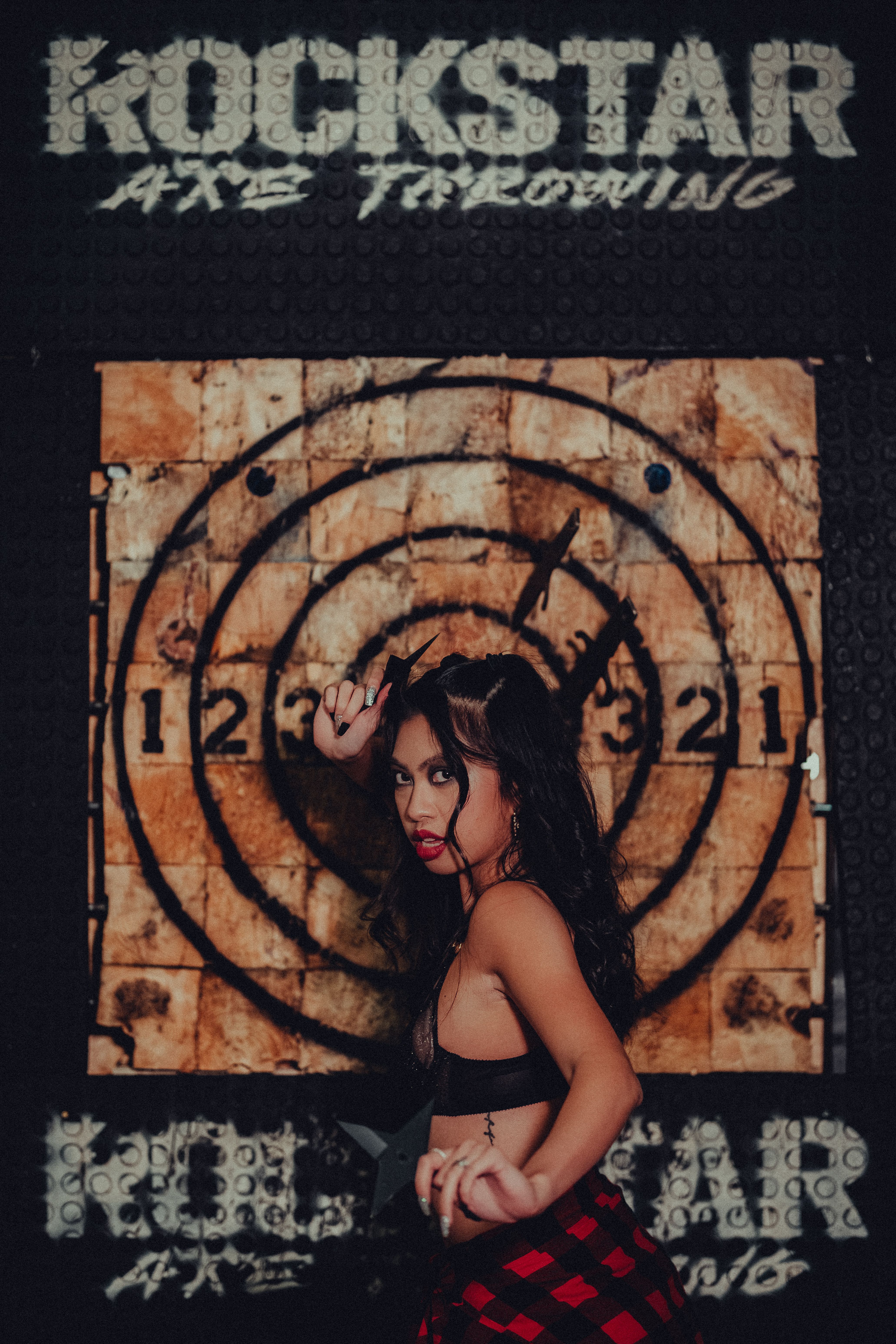 Woman posing confidently in front of an axe throwing target, creating a bold and edgy vibe.