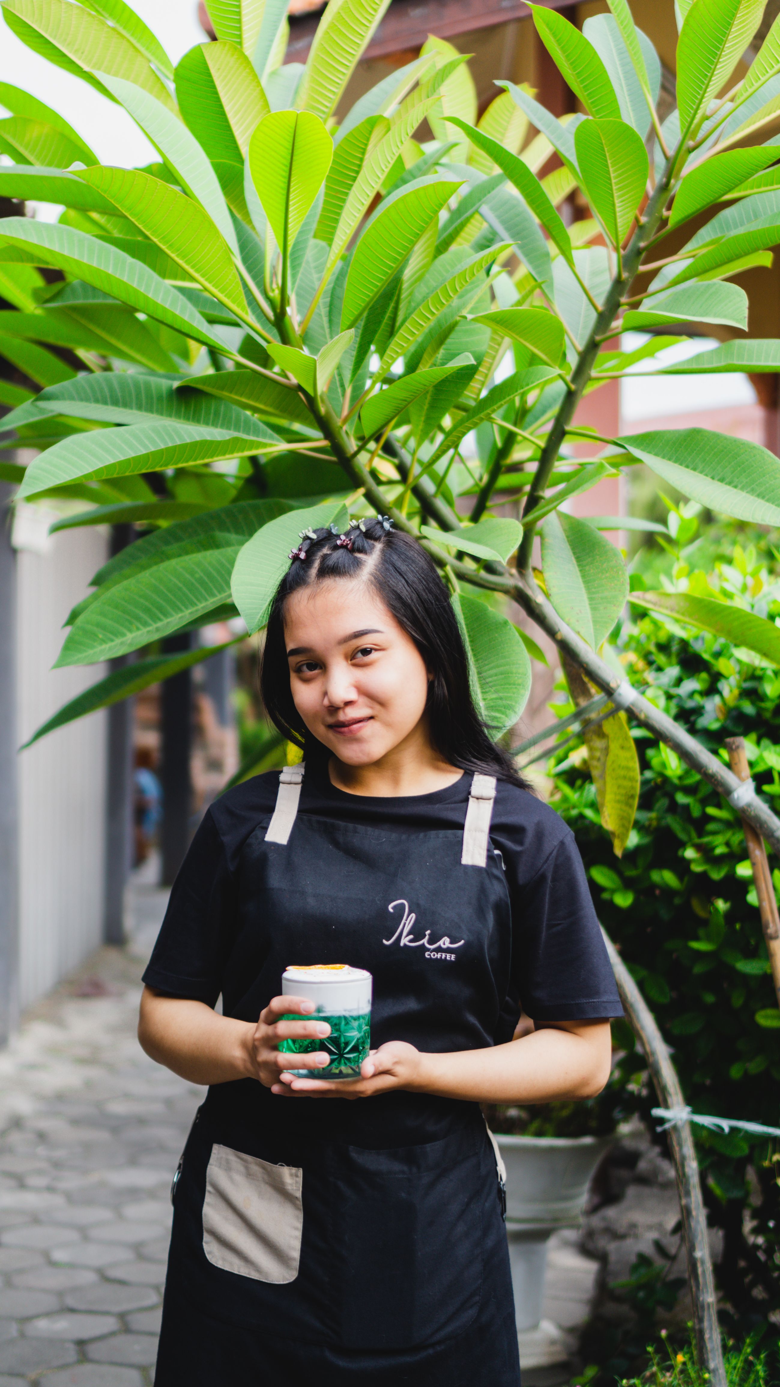 Young barista in black uniform holding coffee outside a cafe in Madiun, Indonesia.