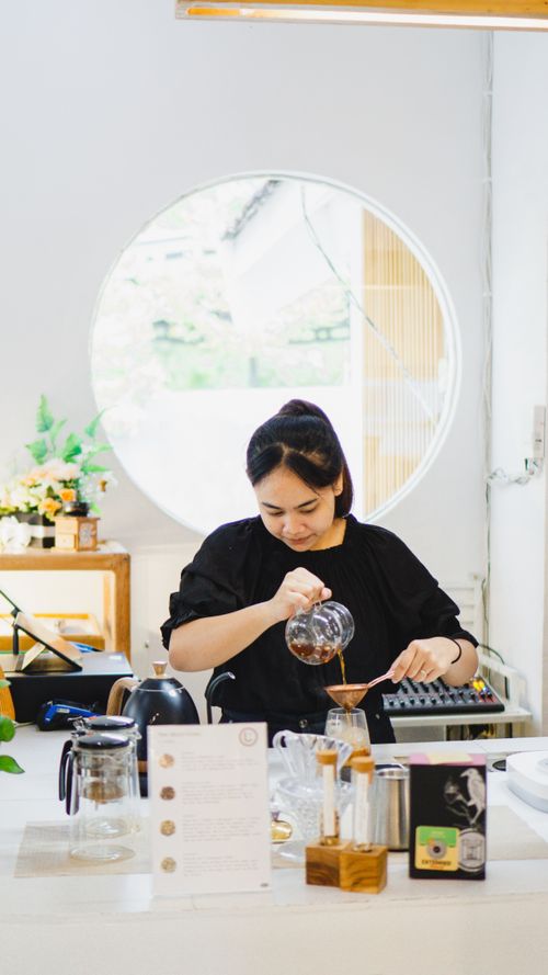 Free Asian woman brews coffee at a café in Madiun, Indonesia, showcasing barista skills. Stock Photo