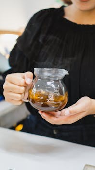 A woman holds a glass pitcher with hot tea, showcasing barista skills.