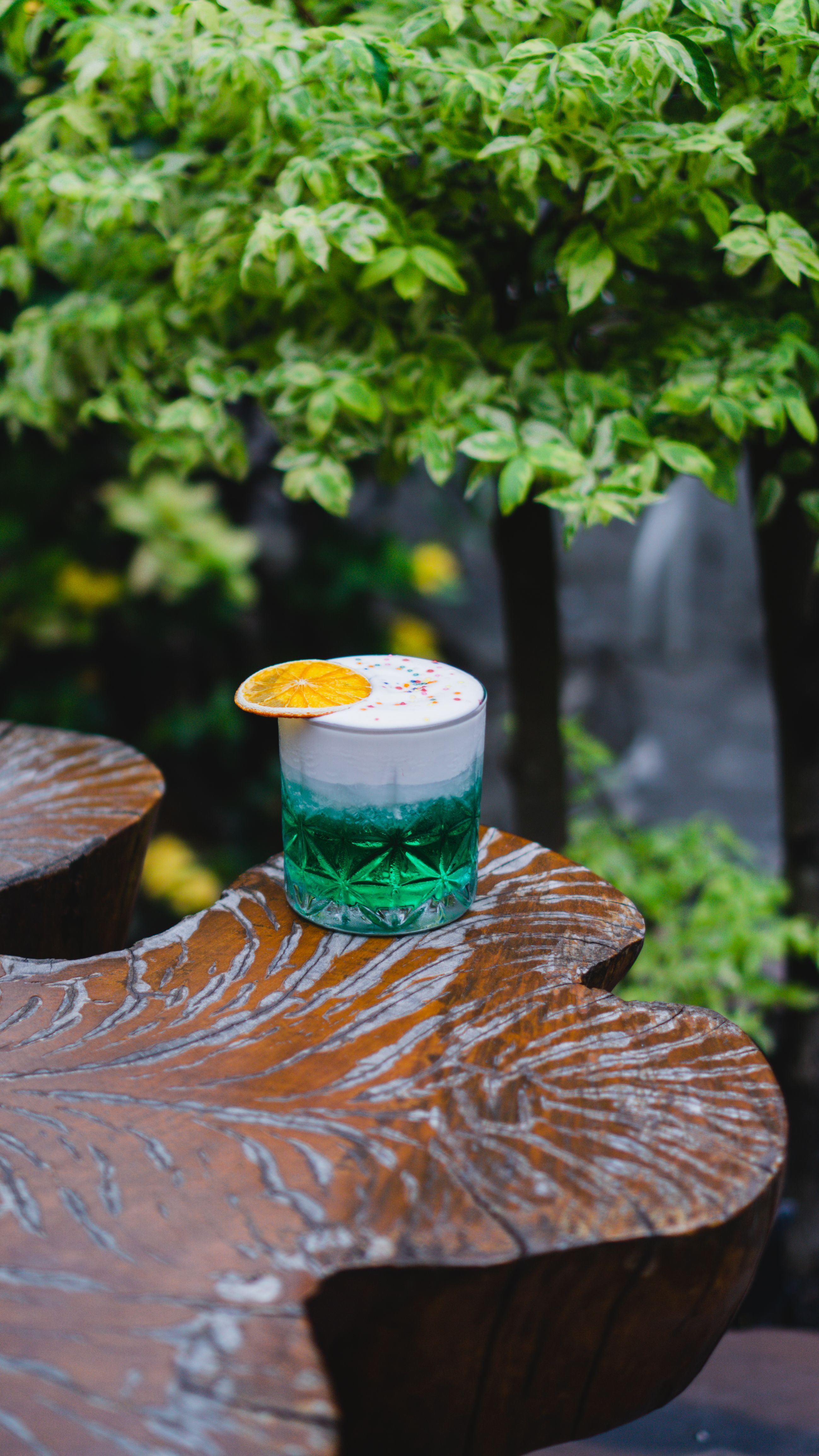 Refreshing colorful cocktail with orange slice garnish on a rustic wooden table outdoors.