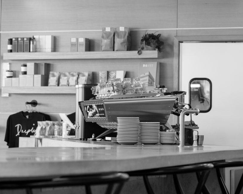 Black and white photo of a modern café with coffee machine and bar counter, showcasing elegant design.
