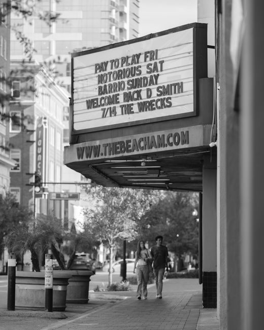 Black and white photo of a downtown street featuring classic cinema signage and people walking.