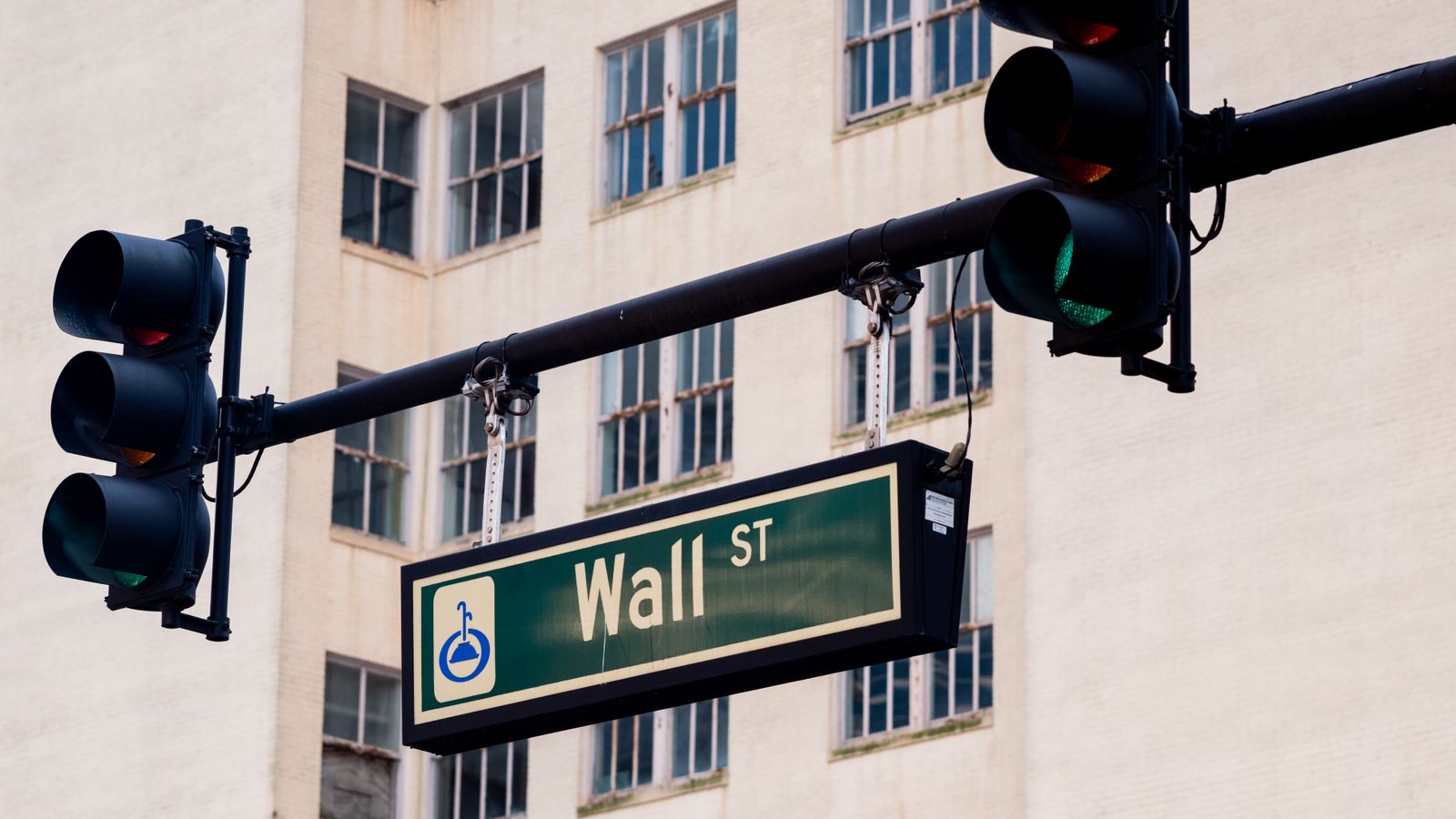 Traffic lights and Wall St sign in cityscape, symbolizing finance hub.