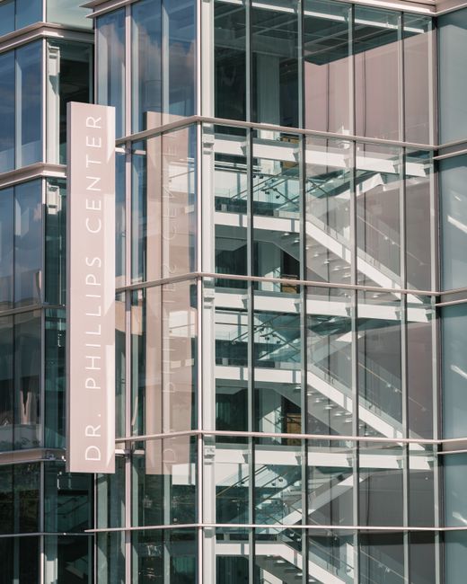 Glass facade of Dr. Phillips Center featuring visible staircases and reflective windows.