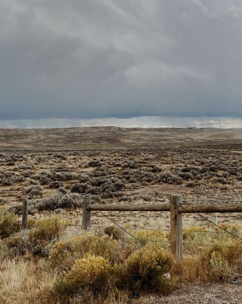 Free Expansive arid landscape with cloudy sky and rustic wooden fence under a dramatic atmosphere. Stock Photo