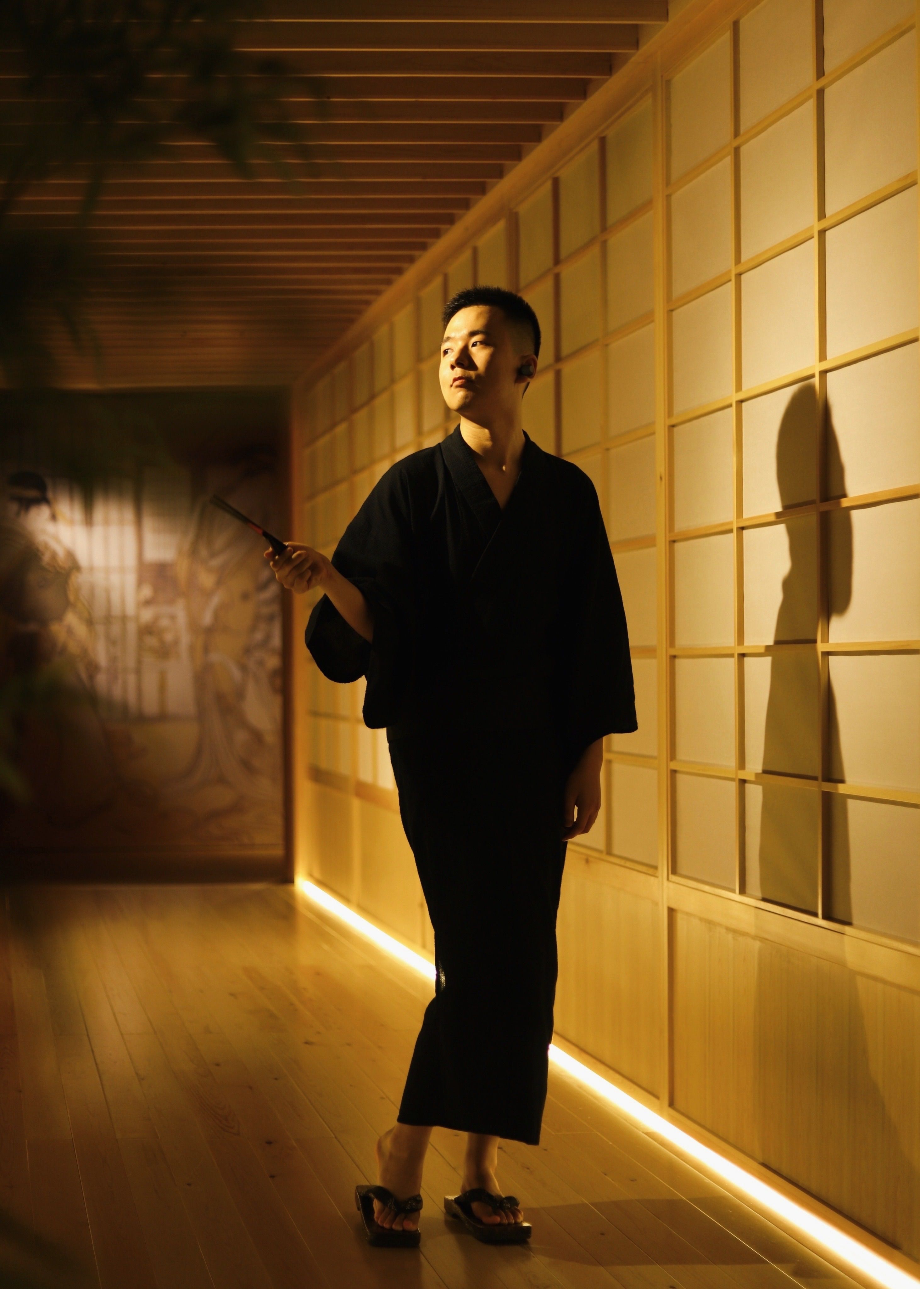An Asian man in a yukata holding an object in a warmly lit traditional room.