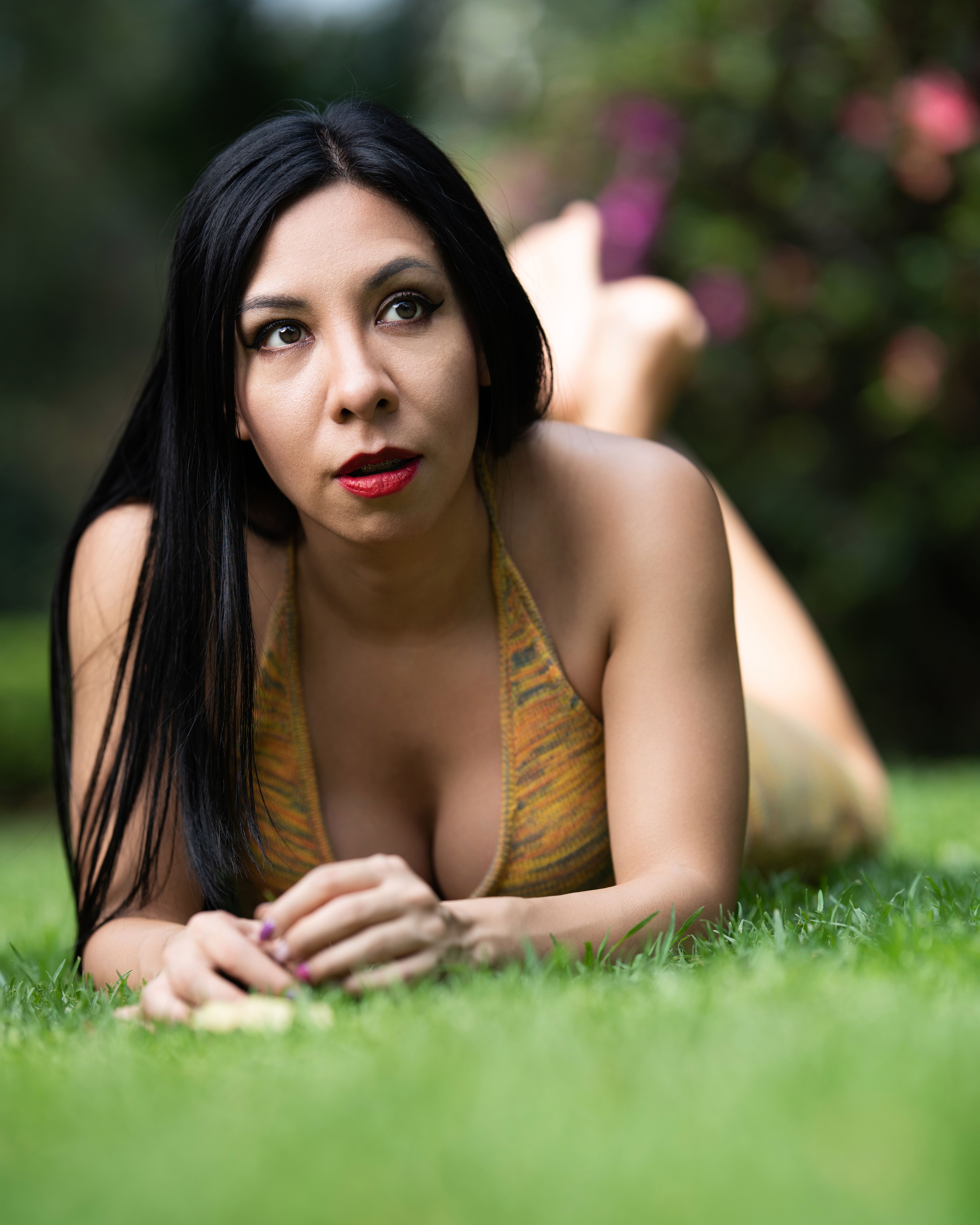 A woman with long dark hair lying on grass, enjoying a peaceful outdoor setting.