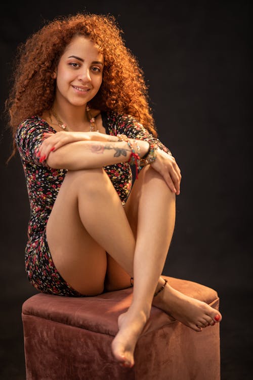 Free Curly-Haired Woman Smiling While Sitting on a Chair Stock Photo