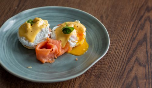 Free Delicious Eggs Benedict topped with creamy hollandaise and smoked salmon on a rustic plate. Stock Photo