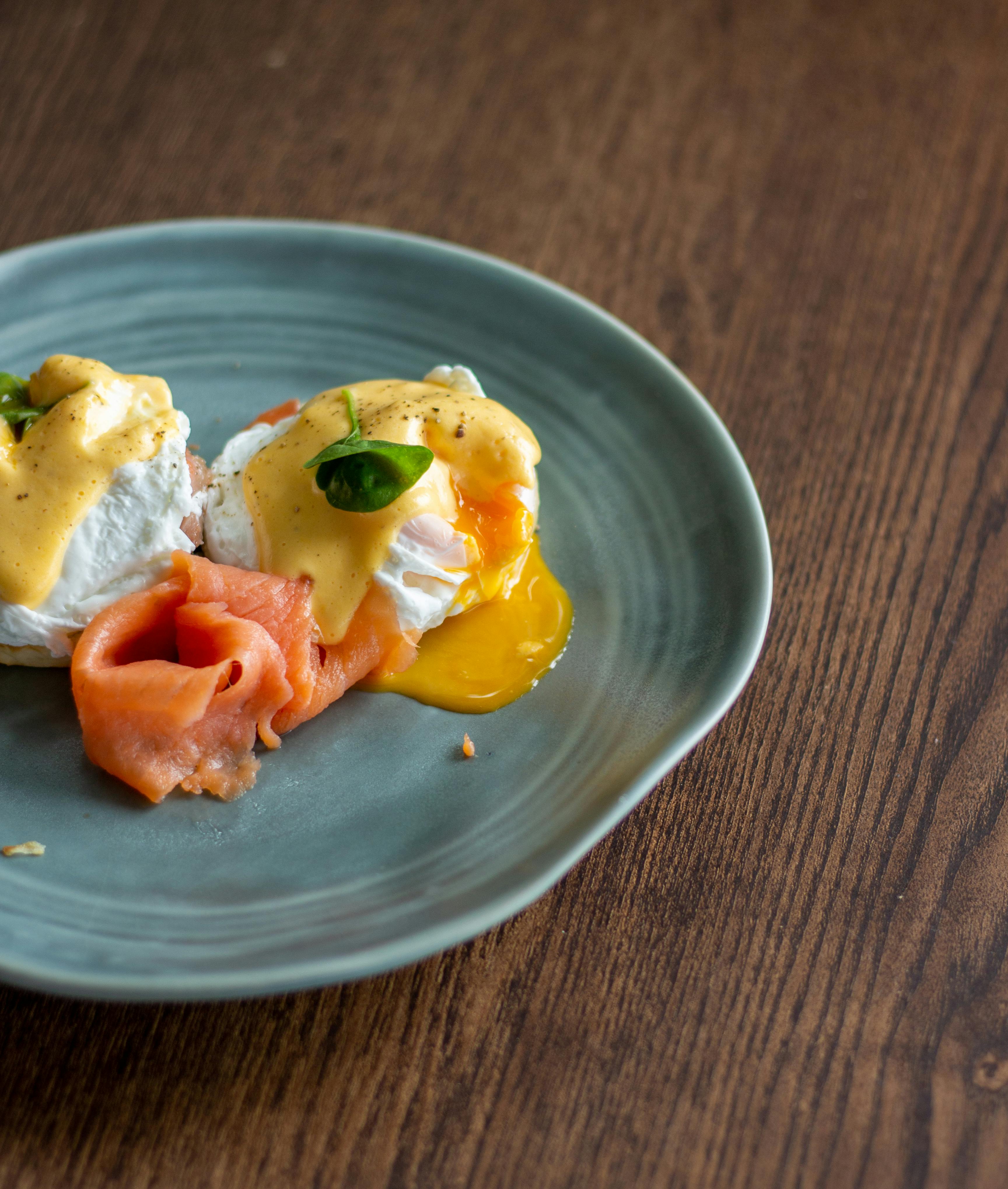 Eggs Benedict with smoked salmon and hollandaise sauce on a ceramic plate on wooden table.
