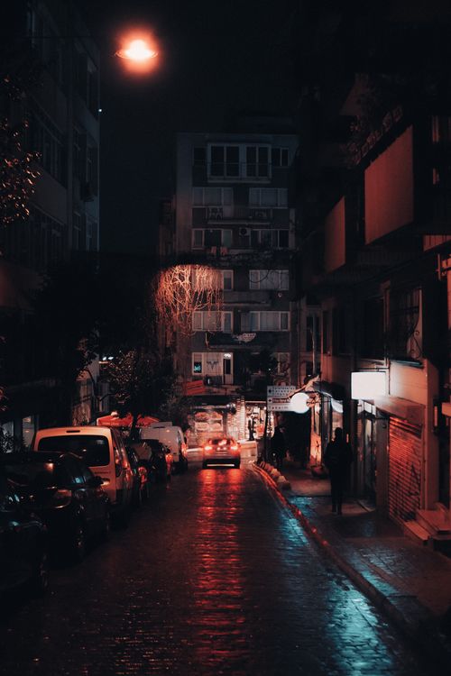 Free Dimly lit urban alley with cars and street lights casting reflections, evoking a moody city atmosphere. Stock Photo