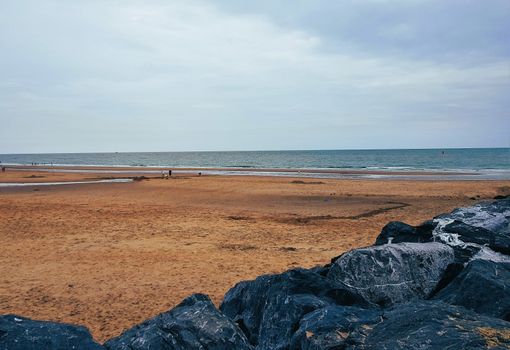 A peaceful sandy beach with rocks and the ocean under a cloudy sky.