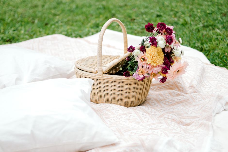 Charming picnic setup with a floral bouquet in a wicker basket on a soft blanket outdoors.