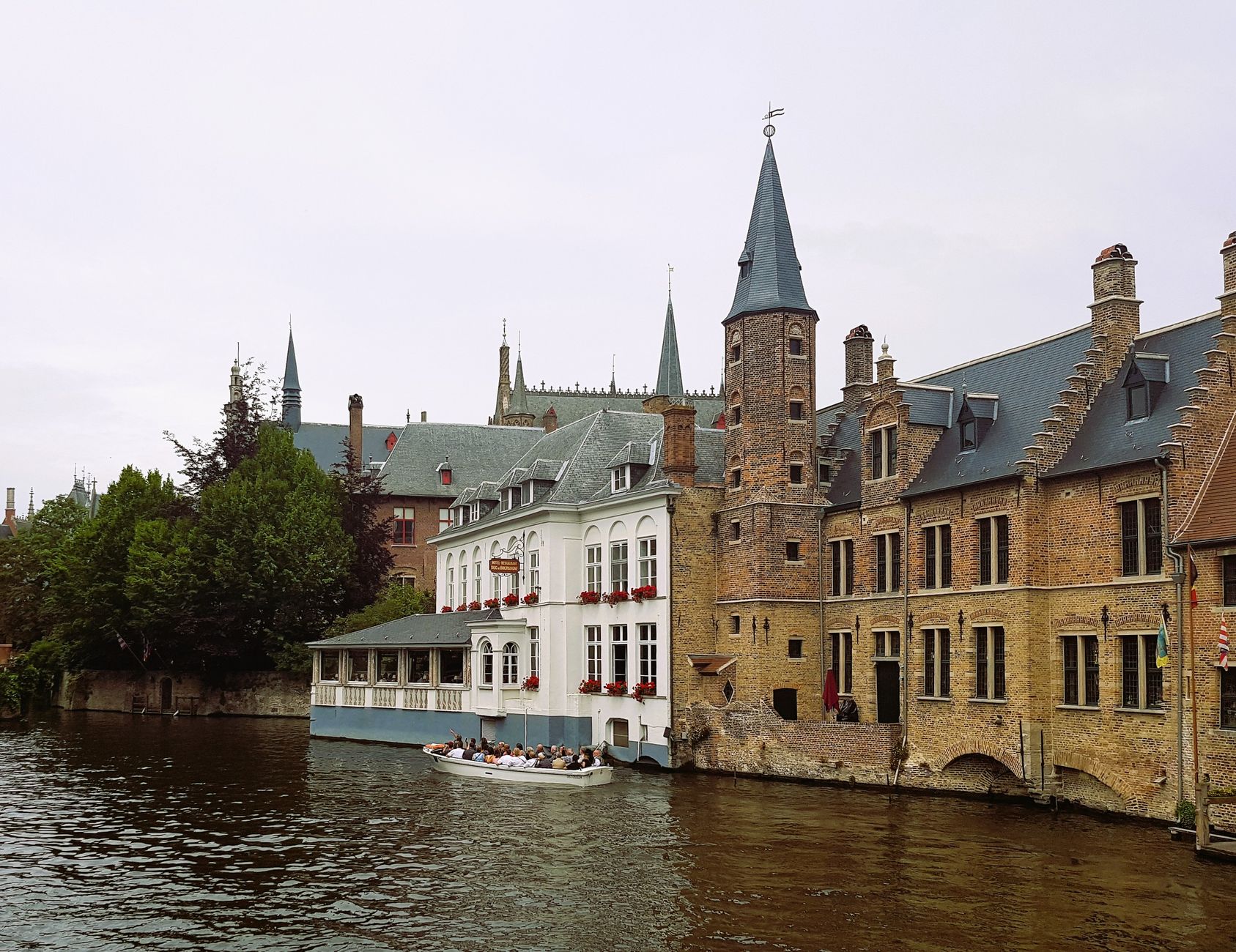 Scenic view of Bruges' historic buildings along a canal with tourists on a boat.