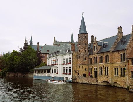Scenic view of Bruges' historic buildings along a canal with tourists on a boat.