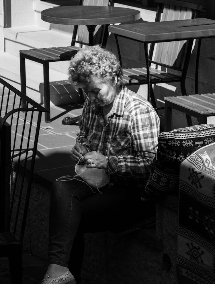 A Woman In Plaid Long Sleeves Sitting On The Street While Knitting Using A Yarn