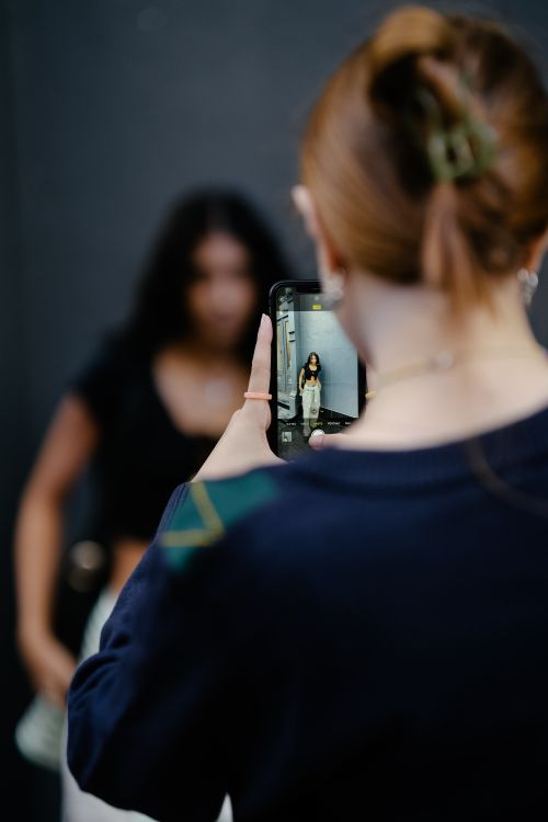 Free A woman captures a photo of another woman using her smartphone outdoors. Stock Photo