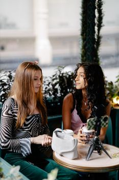 Two young women vlogging and enjoying coffee at a stylish café.