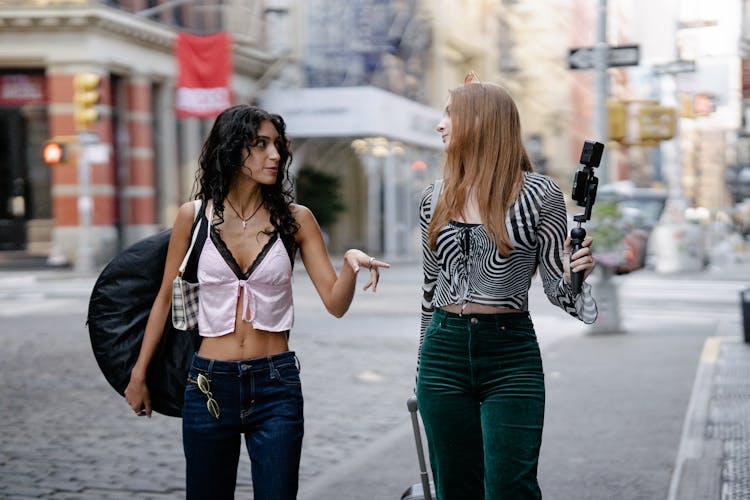 Young Girls Walking In City With Luggage And Camera On A Tripod 