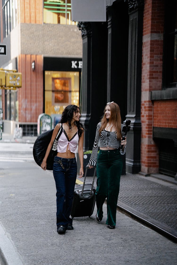 Young Girls Walking In City With Luggage And Camera On A Tripod 