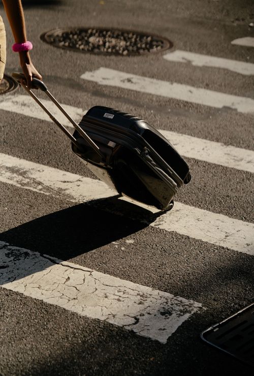 Free Person pulling suitcase across city crosswalk on a sunny day. Stock Photo