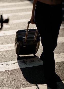 Silhouette of a person crossing a street with a wheeled suitcase, highlighting urban travel vibes.