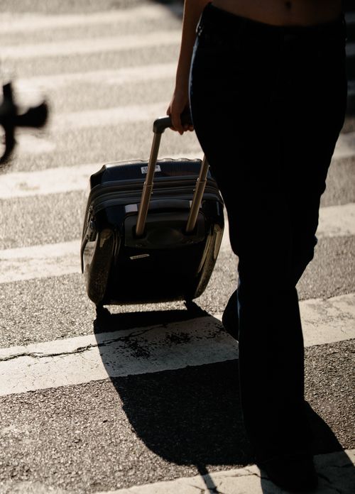 Free Silhouette of a person crossing a street with a wheeled suitcase, highlighting urban travel vibes. Stock Photo