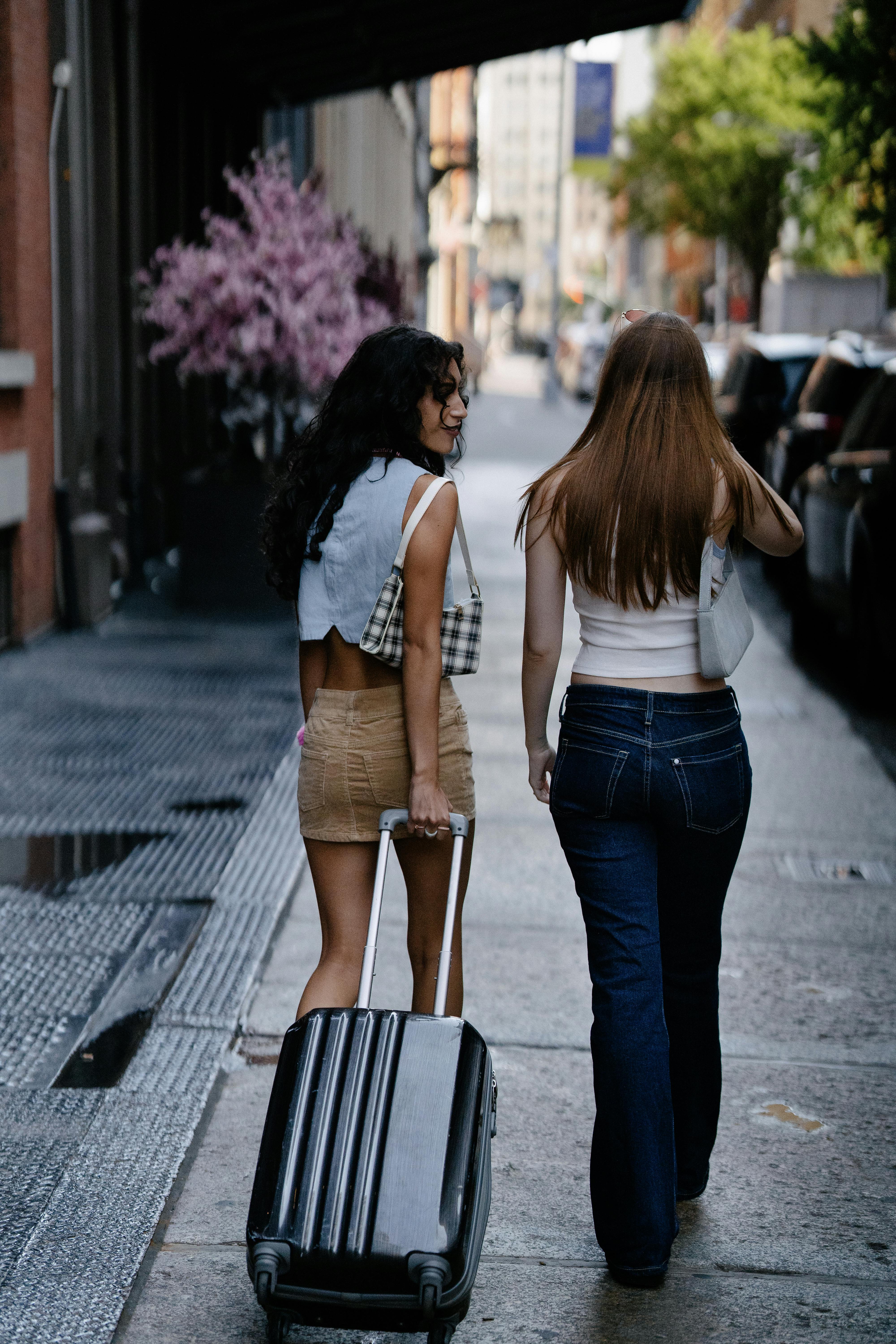 back view of young girls walking on a sidewalk with a suitcase