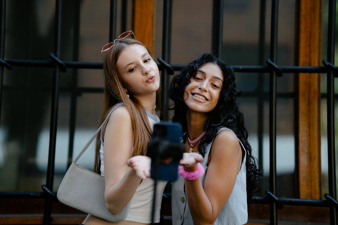 Free Young Fashionable Girls Taking a Picture with a Smartphone on a Tripod Stock Photo