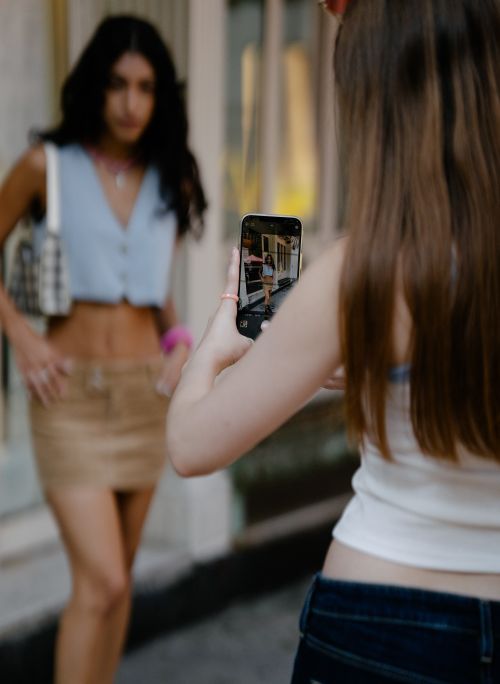 Free Two young women capturing a stylish moment using a smartphone on a vibrant city street. Stock Photo