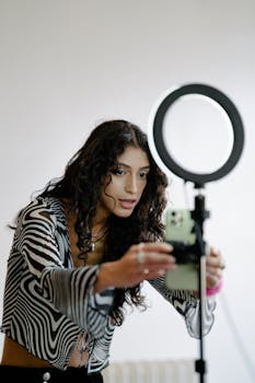 Woman adjusts smartphone on tripod with ring light indoors, perfect lighting for video content.