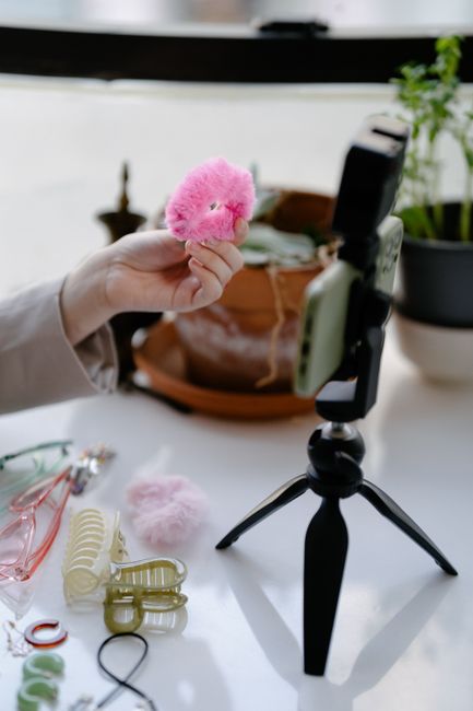 Close-up of a hand showing a pink hair accessory near a smartphone on a tripod.