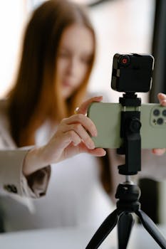 Young woman adjusting smartphone on tripod for photography indoors.