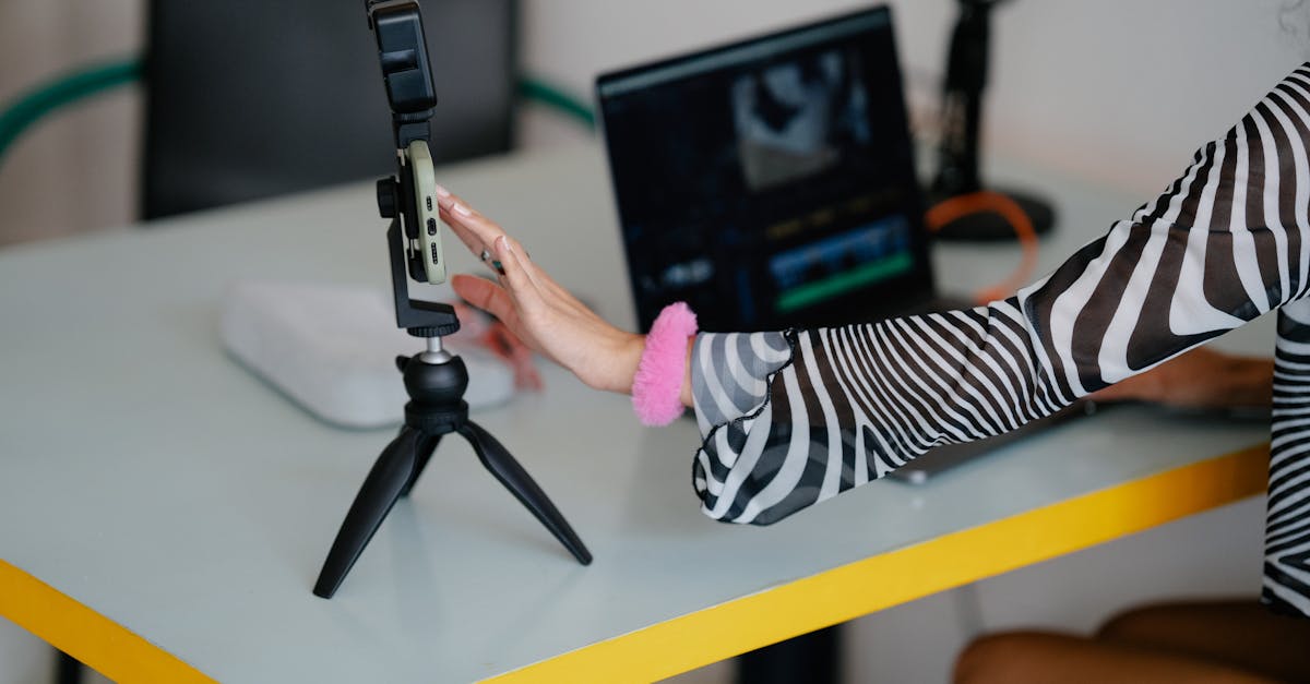 Woman adjusting smartphone on tripod with laptop setup for video editing.