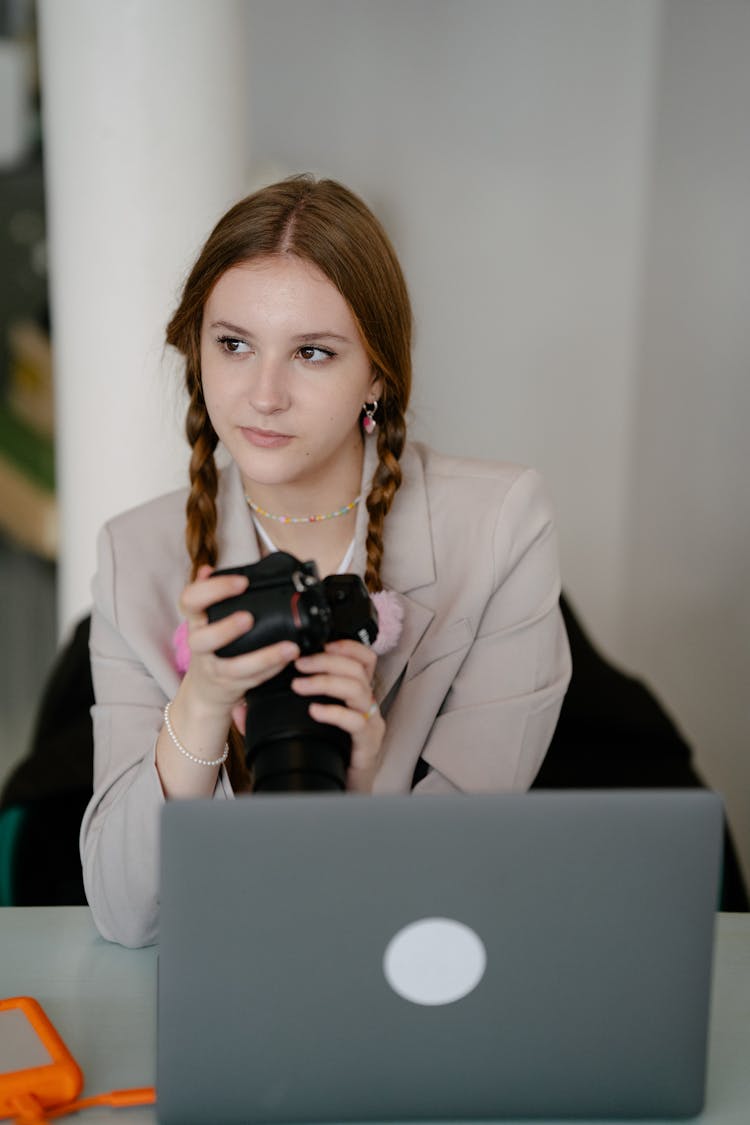 Woman Sitting In Front Of A Laptop And Holding A Camera 