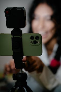 A woman engages with her smartphone mounted on a tripod, smiling as she interacts with the device.