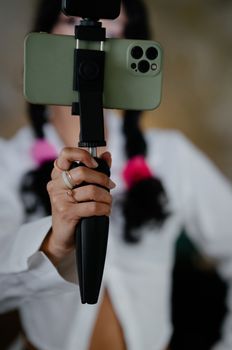 Close-up of a woman's hand holding a smartphone mounted on a tripod, focusing on modern technology.