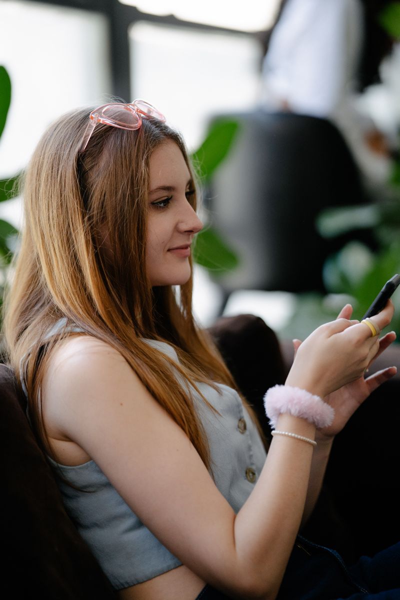 Smiling woman with long hair using phone indoors, casual and relaxed mood.