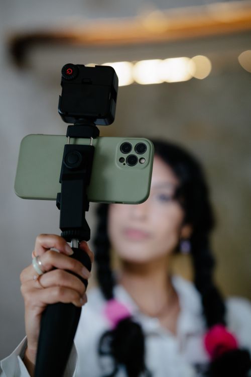 Free Woman with braided hair using a smartphone on a tripod for video recording indoors. Stock Photo